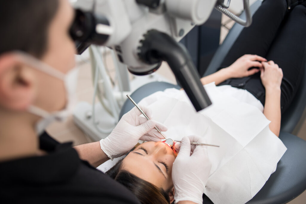 Male dentist with dental tools – microscope, mirror and probe checking up patient teeth at dental clinic office. Medicine, dentistry and health care concept. Dental equipment