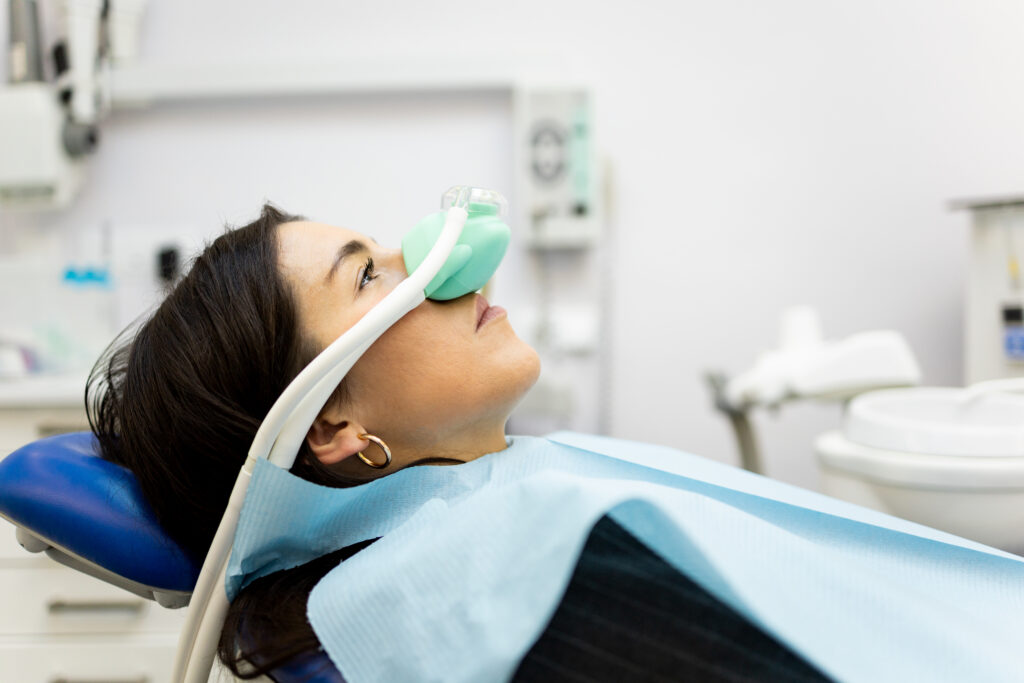 An adult woman sits in a dentist’s office wearing a nasal mask to inhale nitrous oxide. Dentist fear concept. Feeling of relaxation with laughing gas. Visit a dentist with relaxation.